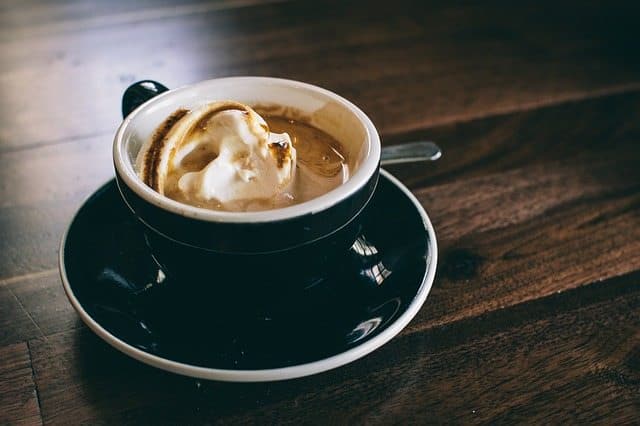 Side view of a cup of coffee with whipped cream on a wood table.